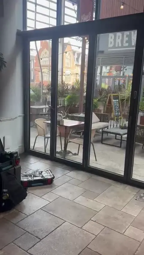 Aluminium bifold doors opening from a bar and kitchen onto its covered outdoor terrace, with the engineer's tools on the floor during the roller and hinge repair