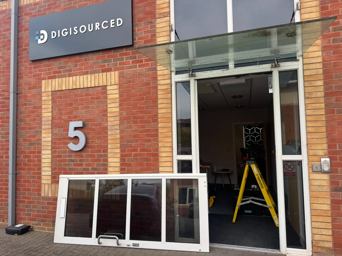 Digisourced office entrance at Unit 5 Tachbrook Park, Warwick, with the white aluminium door leaf removed and standing under the glass canopy during transom closer replacement