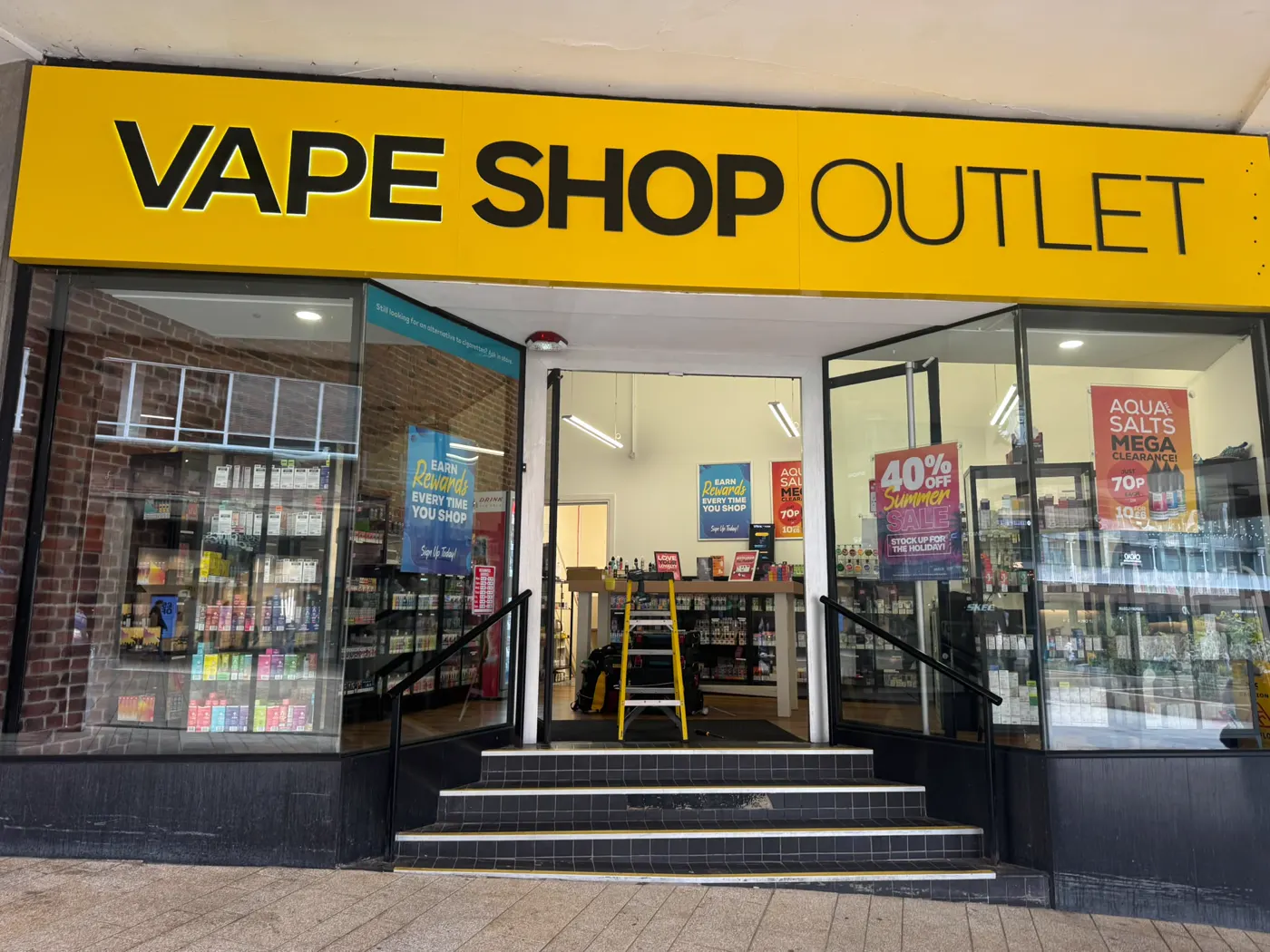 Vape Shop Outlet store front in Coventry with the glass entrance door open and a stepladder inside during floor spring replacement