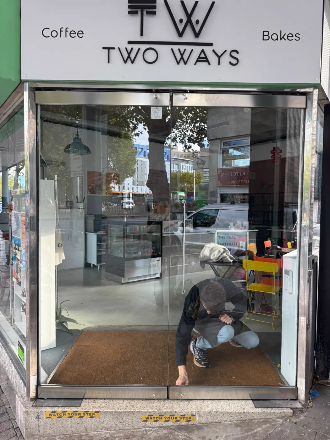 New pair of frameless APG glass doors with stainless rails on the corner entrance of Two Ways coffee and bakes in Bristol, engineer crouched at the bottom rail